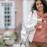 girl outside on college campus smiling while holding her cup of coffee walking to class