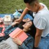 man and woman picnicing woman laying back with book on her chest smiling at male companion